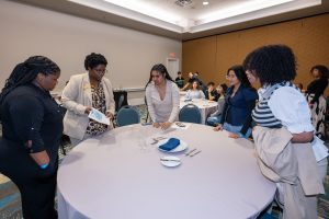 Director of Food & Beverage Adrienne Lee and students review a proper table setting on a large round table.